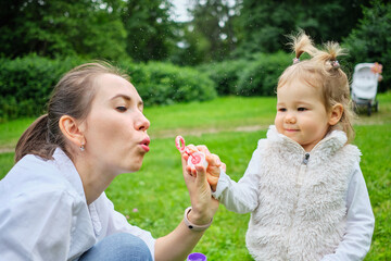 Happy child with mom blows soap bubbles