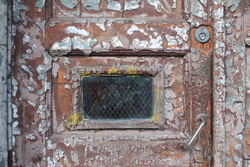 Old wooden door with shabby paint, handle and a small window in the middle
