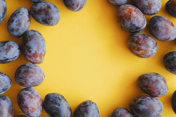 Ripe plums on yellow background, copy space.