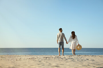 Young couple walking on beach near sea, back view. Honeymoon trip
