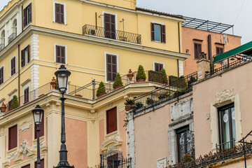 Fototapeta na wymiar Balconies and windows with potted plants. Beautiful yellow and pink colors with details of houses in Rome, Italy.