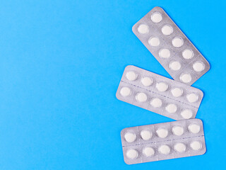 white pills on blue background
Three packs of white pills lie on the right against a blue paper background with space for text on the left, top view close-up.
