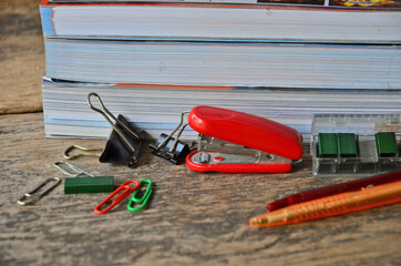 Red stapler and paper clips beside book heap on wooden floor