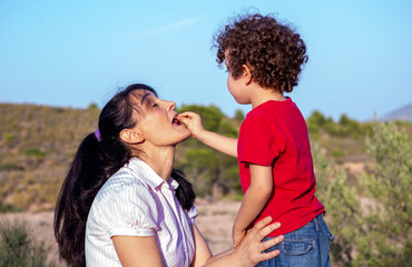 four-year-old boy sticking a cherry in his mom's mouth, on family picnic outing