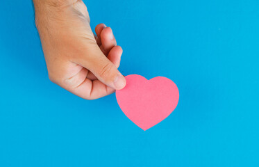 Fototapeta premium Relationship concept on blue background flat lay. hand holding paper cut heart.
