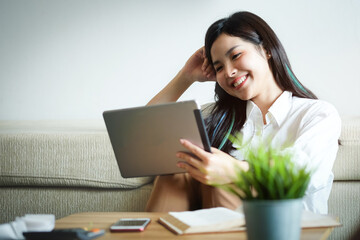 Woman hold with tablet at sit on sofa and use tablet happily at home.