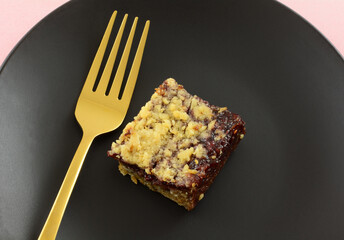 Raspberry oat snack bar on black plate with gold fork