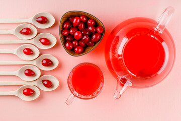 Dogwood berries with drinks in wooden spoons and bowl on pink background, flat lay.