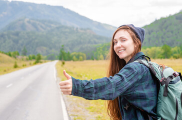 Smiling young woman hitchhiking along a road. Empty space for text