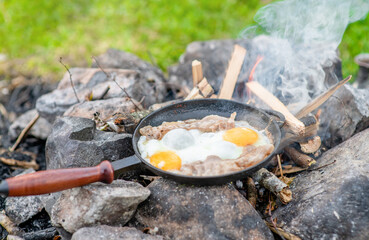 Frying pan with fried eggs and bacon is on the fire in nature