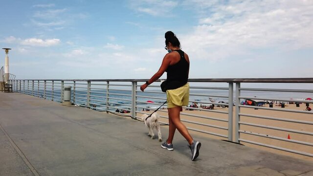 Hispanic woman walking Maltese dog pet along Hermosa Beach Pier, California