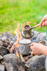 Hiker pours hot coffee from a turkish cezve near a bonfire. Empty space