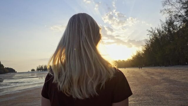 young blonde woman walking towards golden sunset, slow-motion