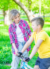 Happy family. Mom talks with her young son who ride a bike in summer park