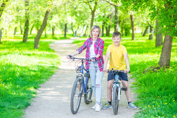 Obraz premium Portrait of mother and son standing with bicycles in sunny summer park. Empty space for text