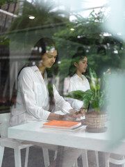View through glass window of two female students concentrating on digital tablet