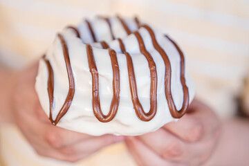 Exquisite homemade cinnamon roll with white coating with hazelnut cream on top held by hands in close up.
