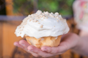 Delicious homemade cinnamon roll covered in white frosting held by one hand.