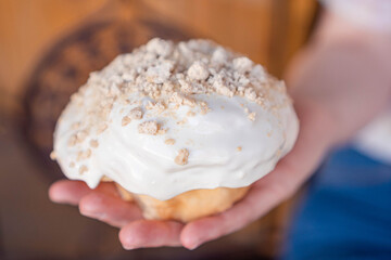 Delicious homemade cinnamon roll covered in white frosting held by one hand.