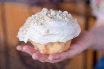 Delicious homemade cinnamon roll covered in white frosting held by one hand.