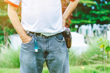 Mini portable alcohol gel bottle to kill Corona Virus(Covid-19) hanging on belt loop of man' s jeans with plants background. New normal lifestyle. Health care concept. Selective focus on alcohol gel