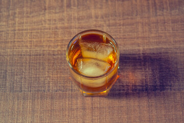 Glass of whiskey or bourbon with ice on a wooden table, top view, for design