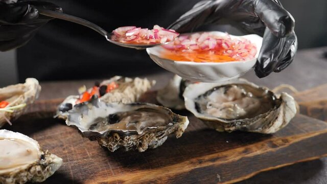 Slow motion sea food video. Big oyster dish. Serving oysters in fish restaurant. Pouring fresh oysters with sauce. Fresh Oyster on half shell on big cutting board in restaurant. Full hd