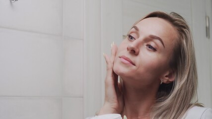 Woman applying cream under the eyes and looking in mirror enjoy natural beauty and healthy