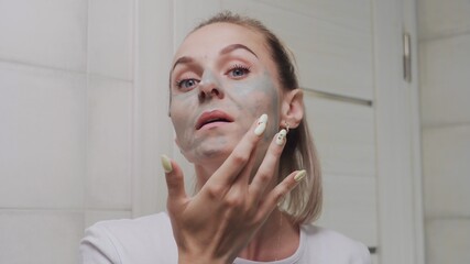 Close up of woman applying clay mask on her face looking at the camera