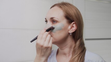 Close up of Adult woman applying clay mask on her face looking in mirror