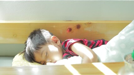 Asian boy is sleeping on the sofa with slow motion of sunlight from curtain