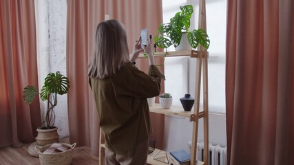 Young woman makes photos of her house plants on shelf