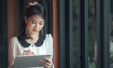 Fototapeta na wymiar Young asian businesswoman working with tablet while standing nera the window glass in modern office.