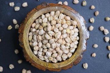 Uncooked dried Chickpeas in a wooden bowl on black background. Preparation for making hummus dish.
High protein ingredient with copy space.  