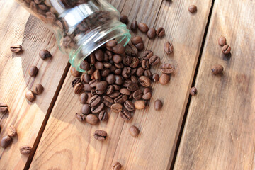 Fresh roasted coffee beans in glass jar on wooden table from above. Scattered coffee beans on wood background with copy space.