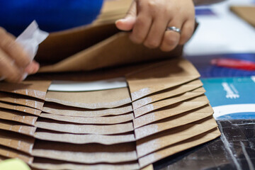 Pila de papeles con pegamento siendo arreglado por una trabajadora en una fábrica que tiene un anillo en la mano - obrazy, fototapety, plakaty