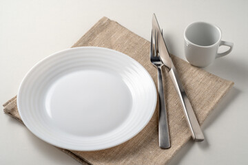 Table setting with a white plate and coffee cup next to cutleries on a white background. Table setting in the restaurant. Empty plate.