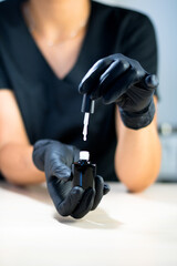 manicurist master in black gloves is holding white nail polish above the table