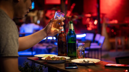 Beer bottles and beer glasses with food on the table with the young man holding the glass and ready to drink in the restaurant.