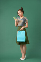 cheerful elegant girl holding shopping bags while chatting on smartphone on green background