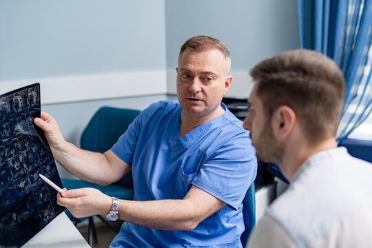 Doctor examining x-ray of a patient. Male radiologist sitting at table. Medical office background.