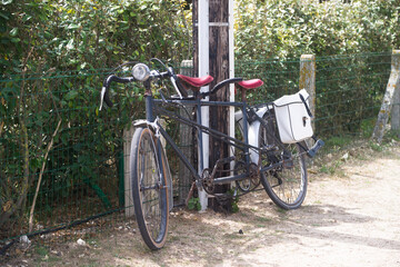Old vintage tandem bike against a wooden electric pole. Two white cycle bag.