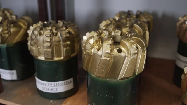 Golden color rock Drill Bits on shelving in stock. Oil drilling equipment for drilling rig operation on oil platform in oil and gas industry. Brand new PDC Polycrystalline Diamond Compact drilling bit