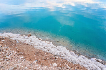 Fototapeta na wymiar Sand covered with crystalline salt on shore of Dead Sea, turquoise blue water near - typical scenery at Ein Bokek beach, Israel