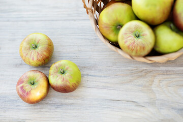 ripe apples lie on a light wooden background and a basket with apples out of focus top view