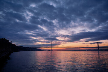 Fototapeta na wymiar Sunset on Tagus river in Lisbon. View on Bridge and Statue of Jesus Christ.