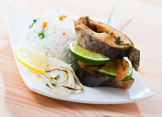 Baked trout steaks with boiled rice and sliced lemon garnished with scallions served on white plate