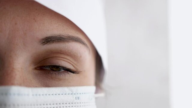 Portrait of a female doctor or nurse wearing medical cap and face mask looking at the camera. Close up of eye. Health care, medical concept. slow motion