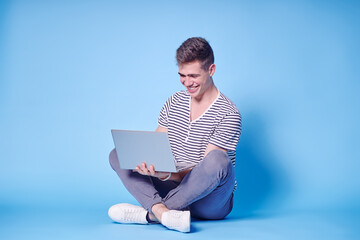 Studio portrait of handsome young man using laptop on blue background.