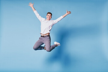 Fototapeta na wymiar Colorful studio portrait of happy young man jumping against blue background.